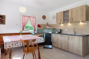 A kitchen with wooden cabinets, a dining table with a checkered tablecloth, and a window with a red curtain.