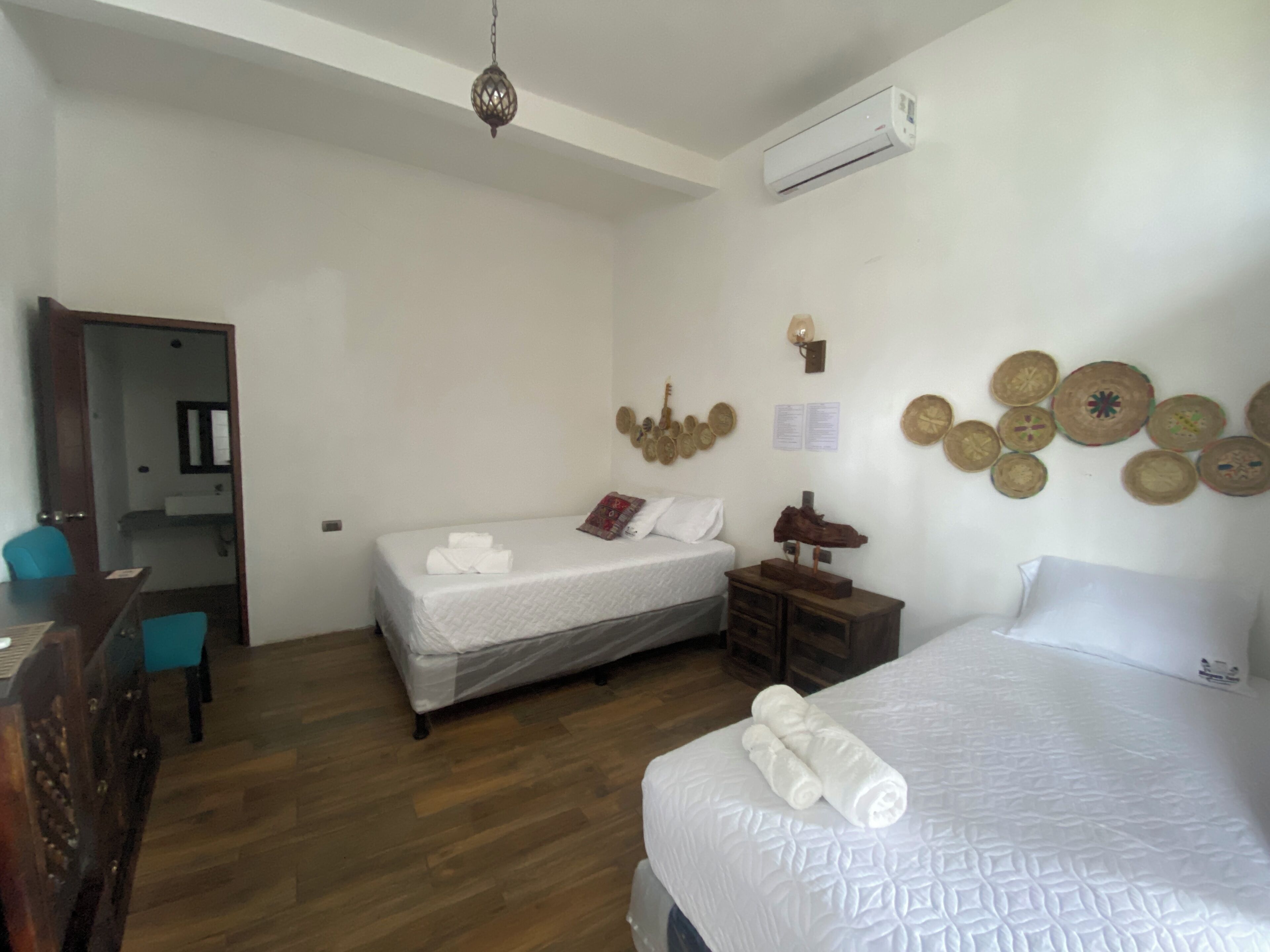 A hotel room with two beds, a wooden floor, a desk with a chair, a wardrobe, and a wall decorated with circular wall hangings.