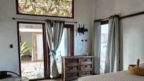 Un dormitorio con una cama, un aparador de madera, una mesa y una ventana con cortinas.