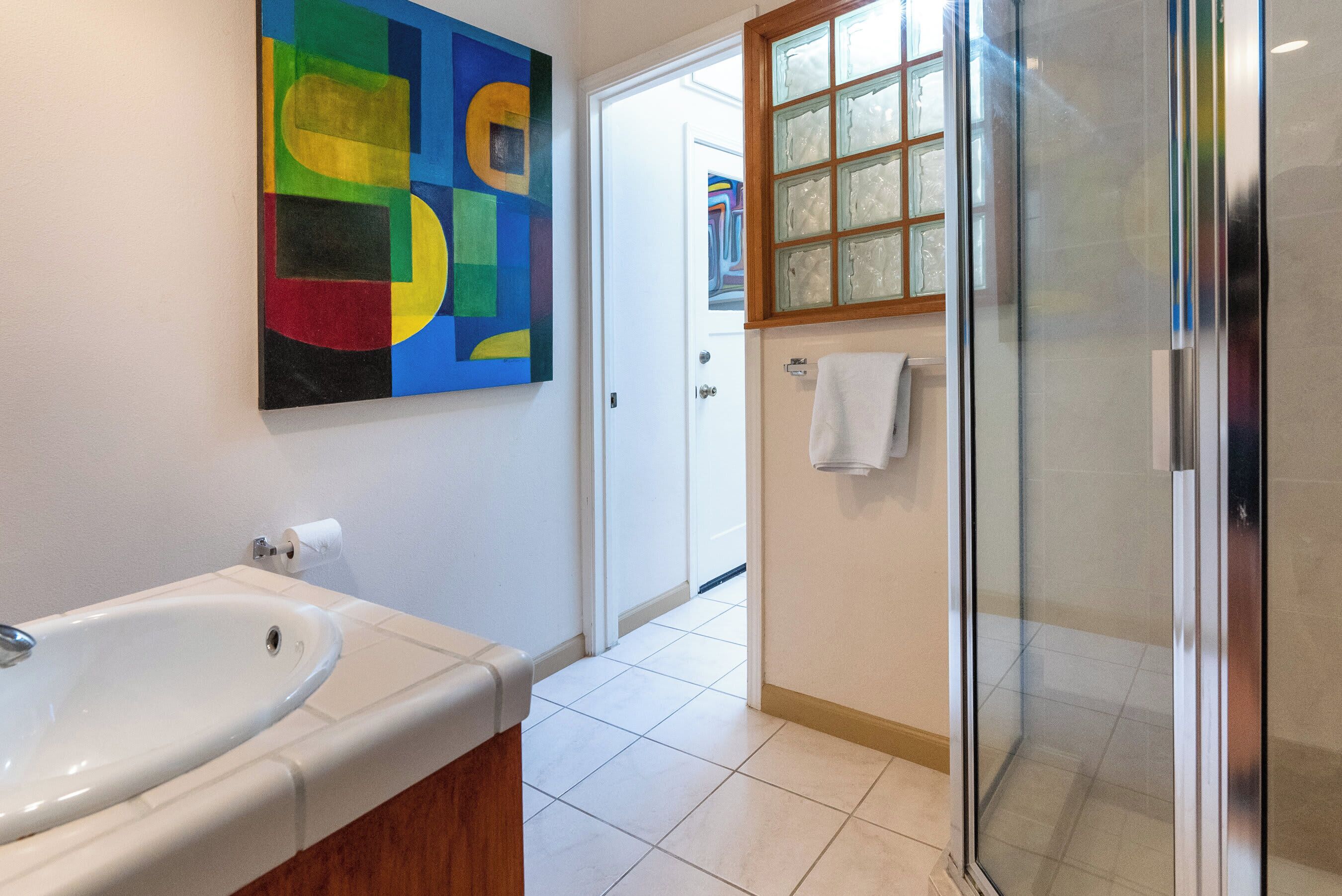 Ein Badezimmer mit einem weißen Waschbecken, einem farbenfrohen abstrakten Gemälde und einer Duschkabine aus Glas.