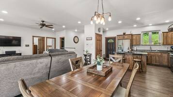 A spacious living room with a large sofa, wooden dining table, and a kitchen area with wooden cabinets and a built-in oven.