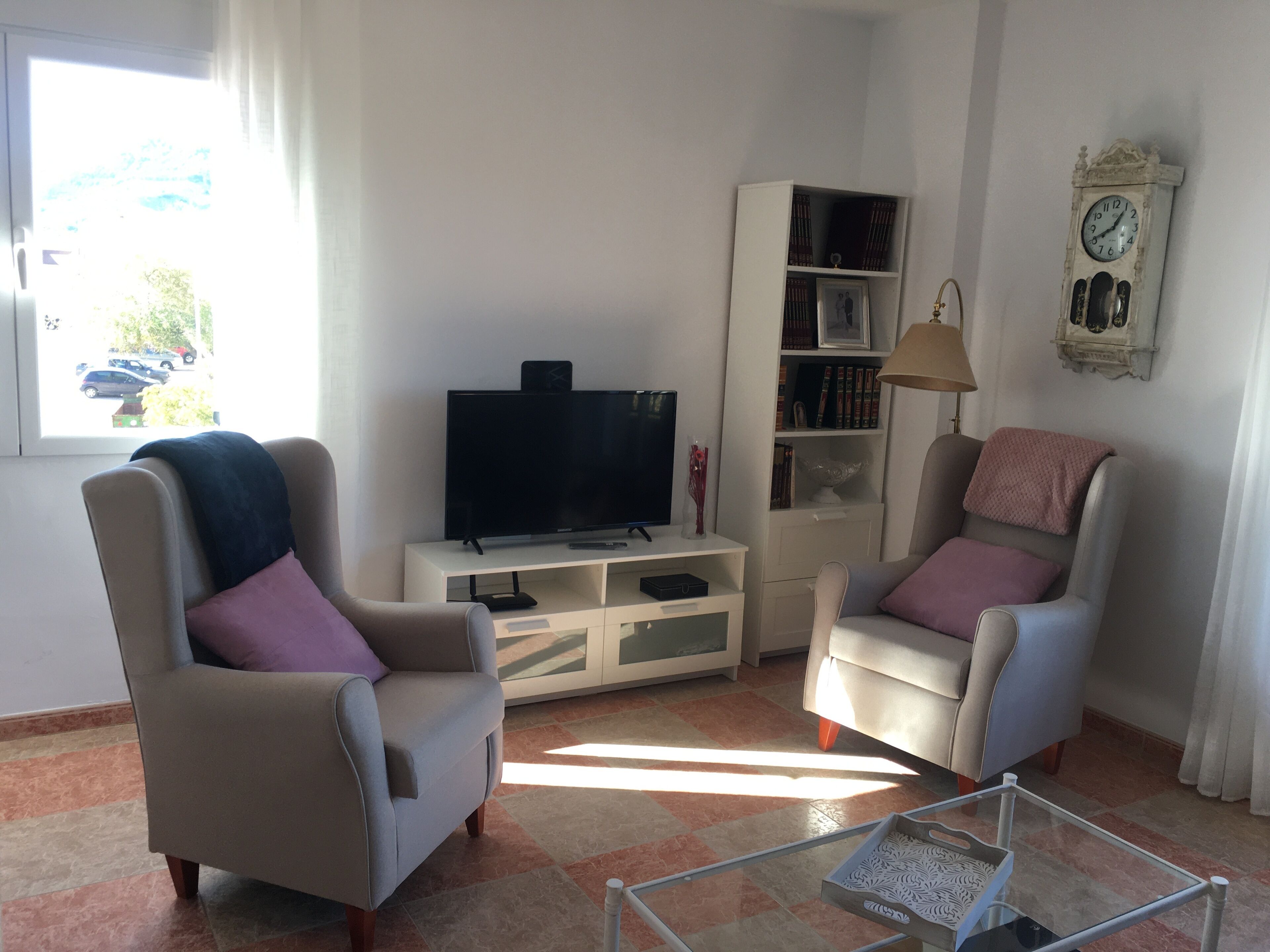 Een woonkamer met twee fauteuils, een televisie, een boekenkast en een klok aan de muur.