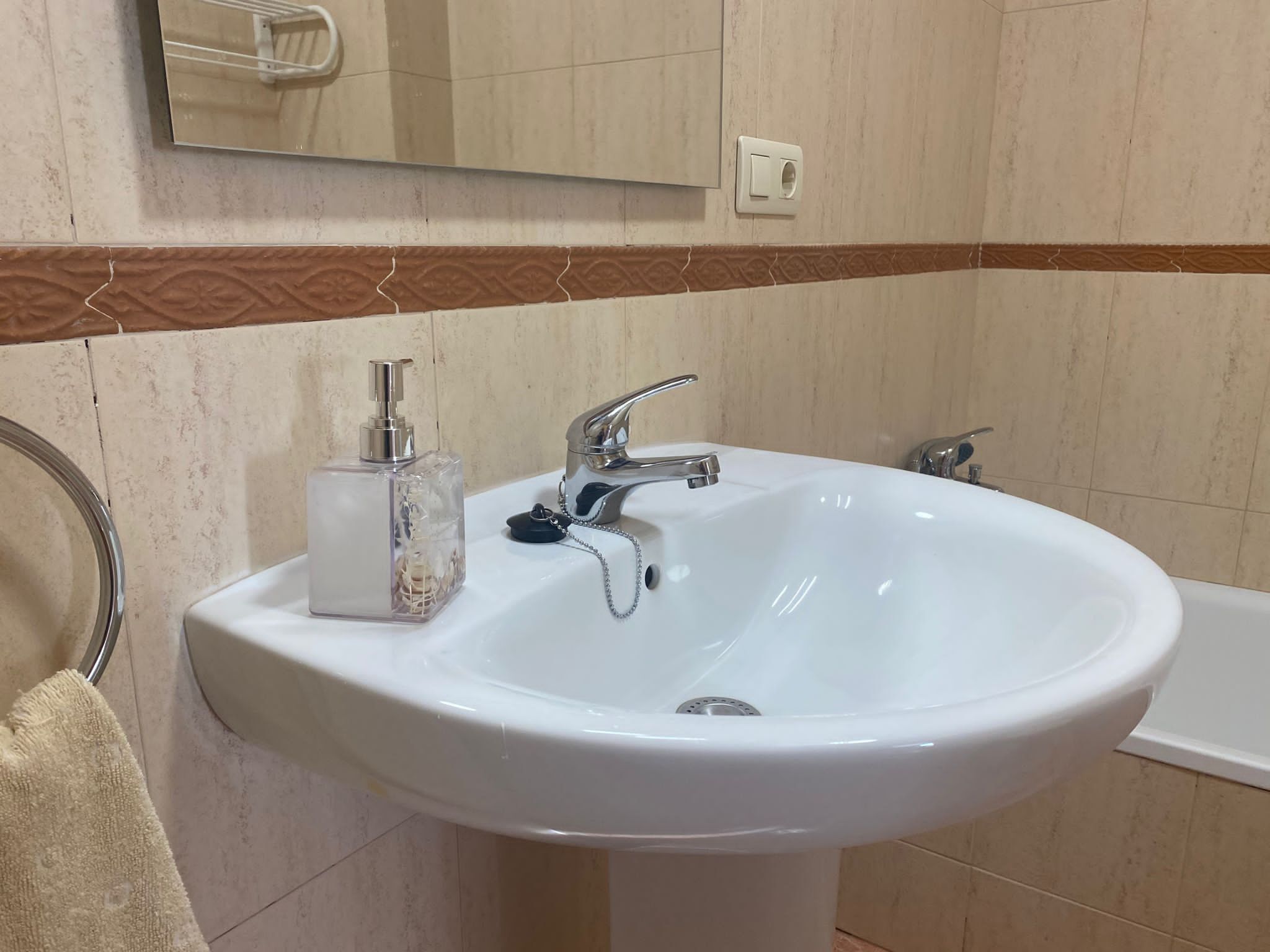 Un baño con un lavamanos blanco, un espejo encima y un perchero a la izquierda.