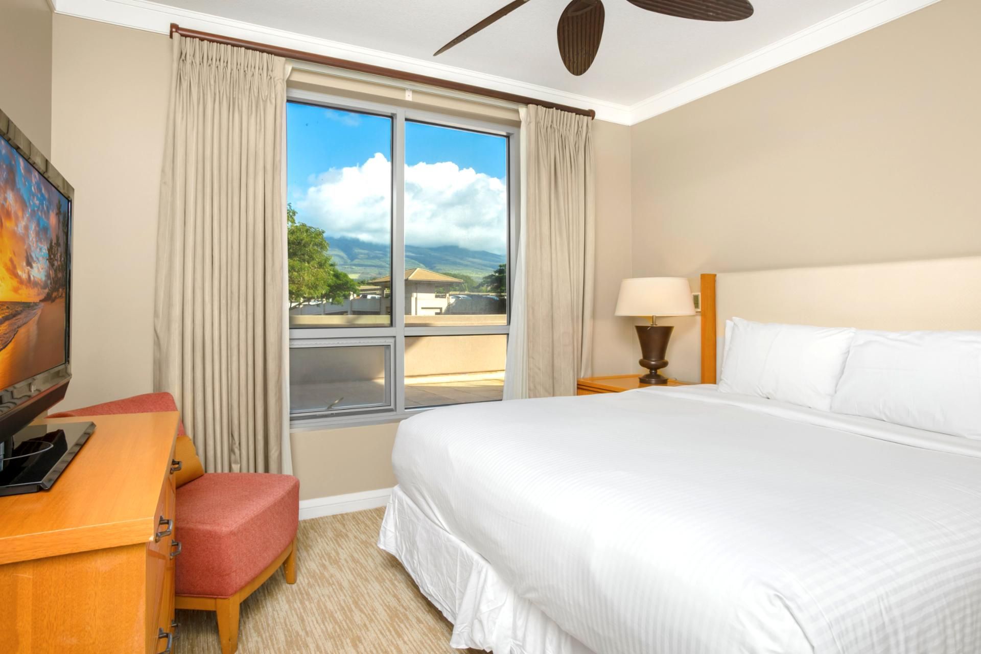 A hotel room with a bed, a desk with a chair, a television, and a window with curtains.