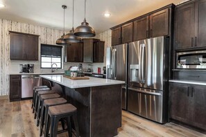 A modern kitchen with dark wood cabinets, stainless steel appliances, and a central island with bar stools.