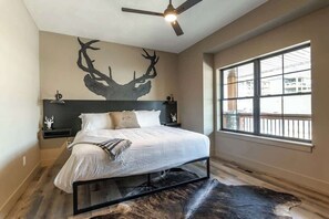 A bedroom with a bed, a ceiling fan, a window, and a wall-mounted deer antler decoration.