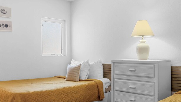 Une chambre à coucher avec un lit, une table de chevet, une lampe, une commode et une fenêtre.