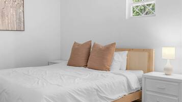A bedroom with a bed, pillows, a nightstand, a lamp, a window, and a wall art piece.