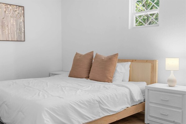 A bedroom with a bed, pillows, a nightstand, a lamp, a window, and a wall art piece. - Enchanted Woods Retreat Branson (Branson)