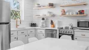 Une cuisine moderne avec des meubles blancs, un réfrigérateur en acier inoxydable, une machine à café et un four à micro-ondes.