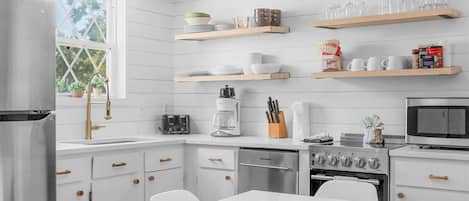 A modern kitchen with white cabinetry, a stainless steel refrigerator, a coffee maker, and a microwave.
