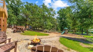 A park with picnic tables, a fire pit, playground equipment, and a wooden structure.