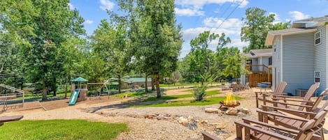 Ein Garten mit Spielplatz, Sitzgelegenheit im Freien und einer Feuerstelle.