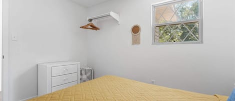 A bedroom with a bed, a dresser, a window, and a wall-mounted fan.