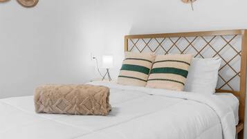 Una cama bien tendida con edredón blanco, dos almohadas con rayas verdes y una manta color beige.
