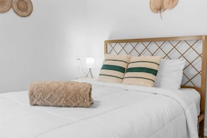 Un lit bien fait, avec une couette blanche, deux oreillers à rayures vertes et un plaid beige.