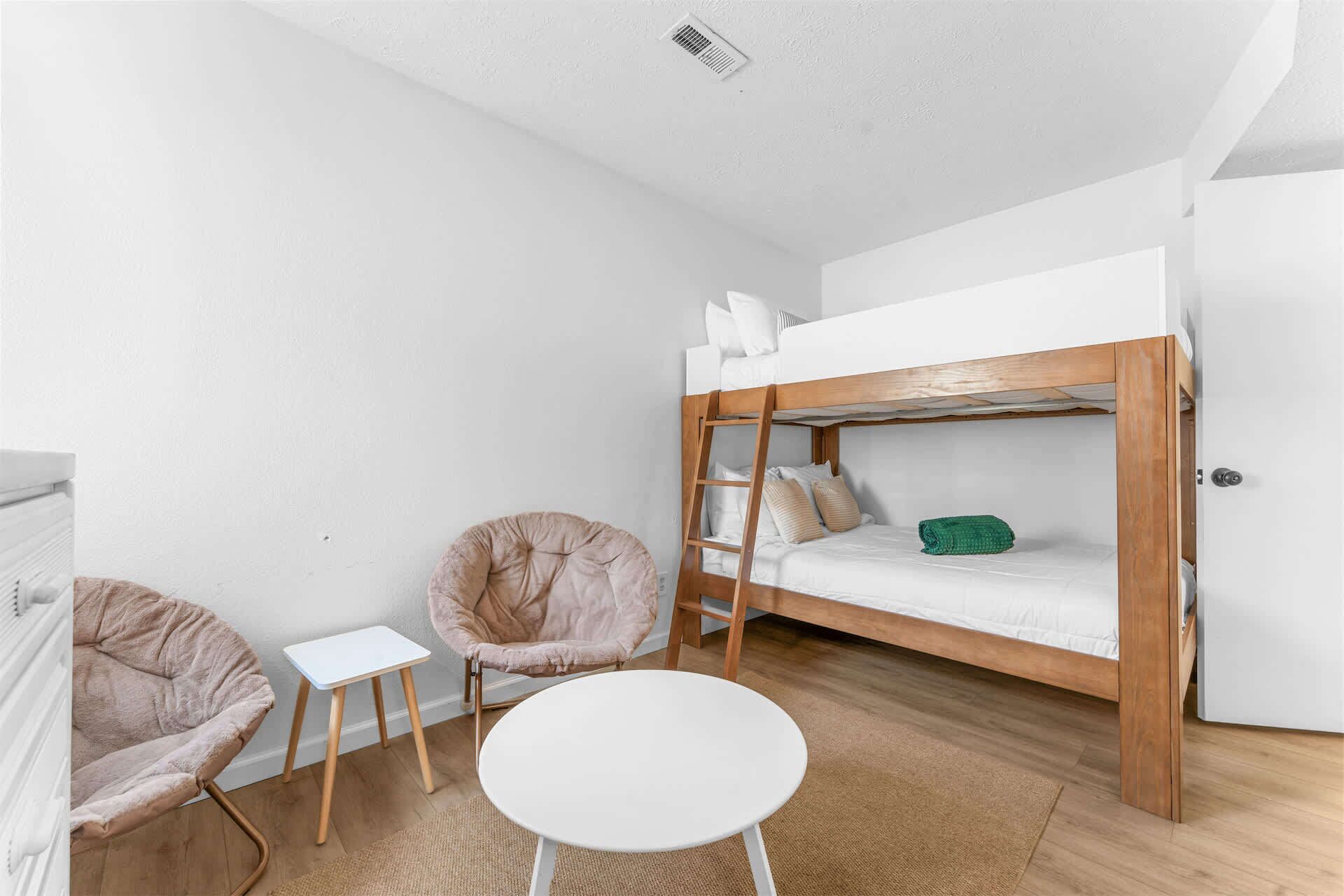 A compact room with a bunk bed, a small round table, a chair, and a radiator.