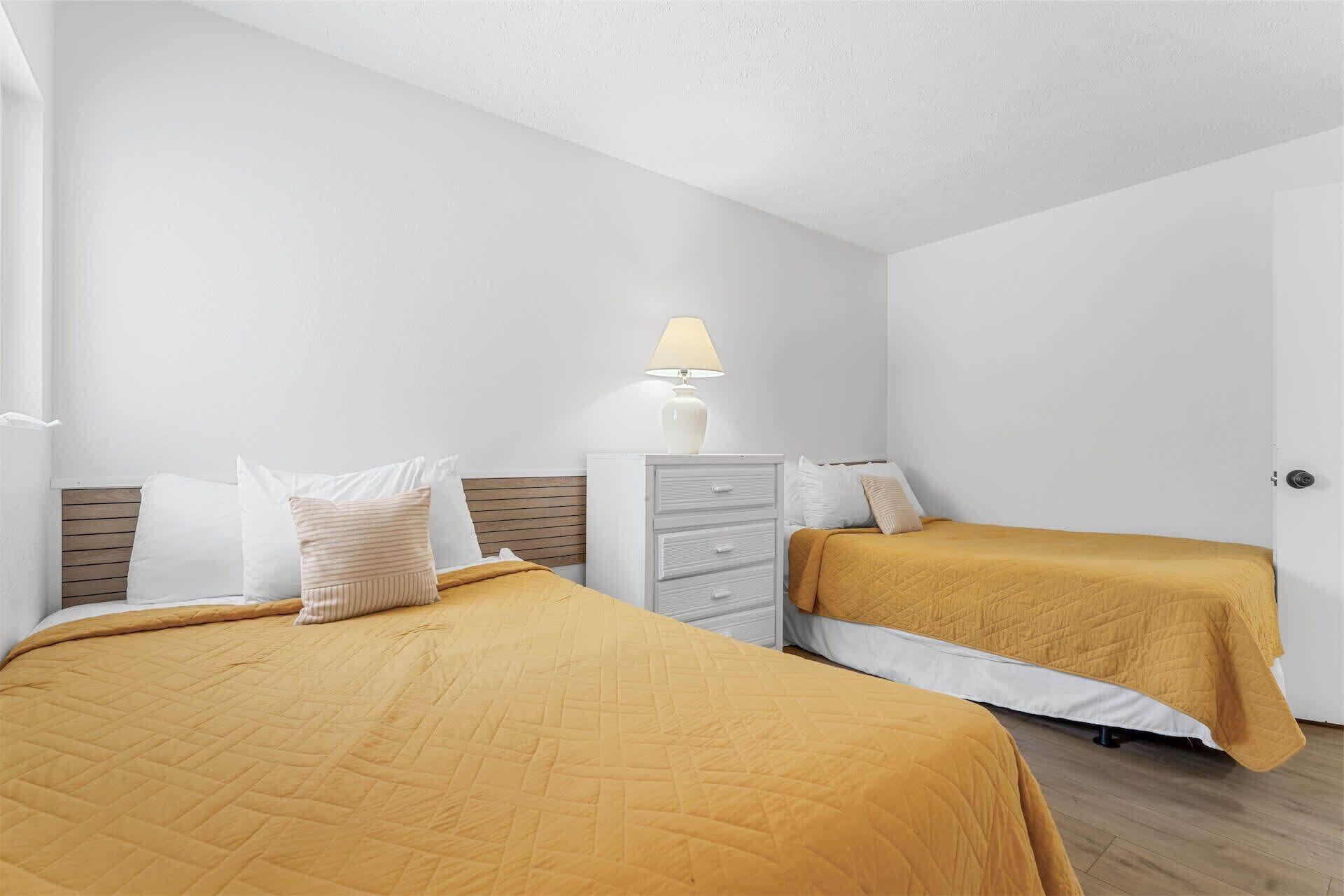 A bedroom with two beds, a nightstand, and a lamp.