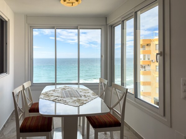 A dining area with a table and chairs, large windows with a view of the ocean, and a ceiling light fixture.