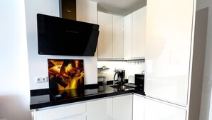 Una cocina moderna con armarios blancos, encimera negra, horno empotrado y cafetera.