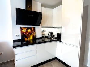 A modern kitchen with white cabinets, a black countertop, a built-in oven, and a coffee maker.