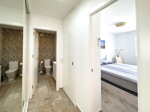 A hotel room with a bed, a bathroom with a toilet and sink, and a hallway leading to another room.