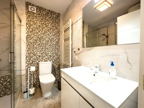 Un bagno con pavimento in marmo, un water, una doccia e un lavandino con specchio.