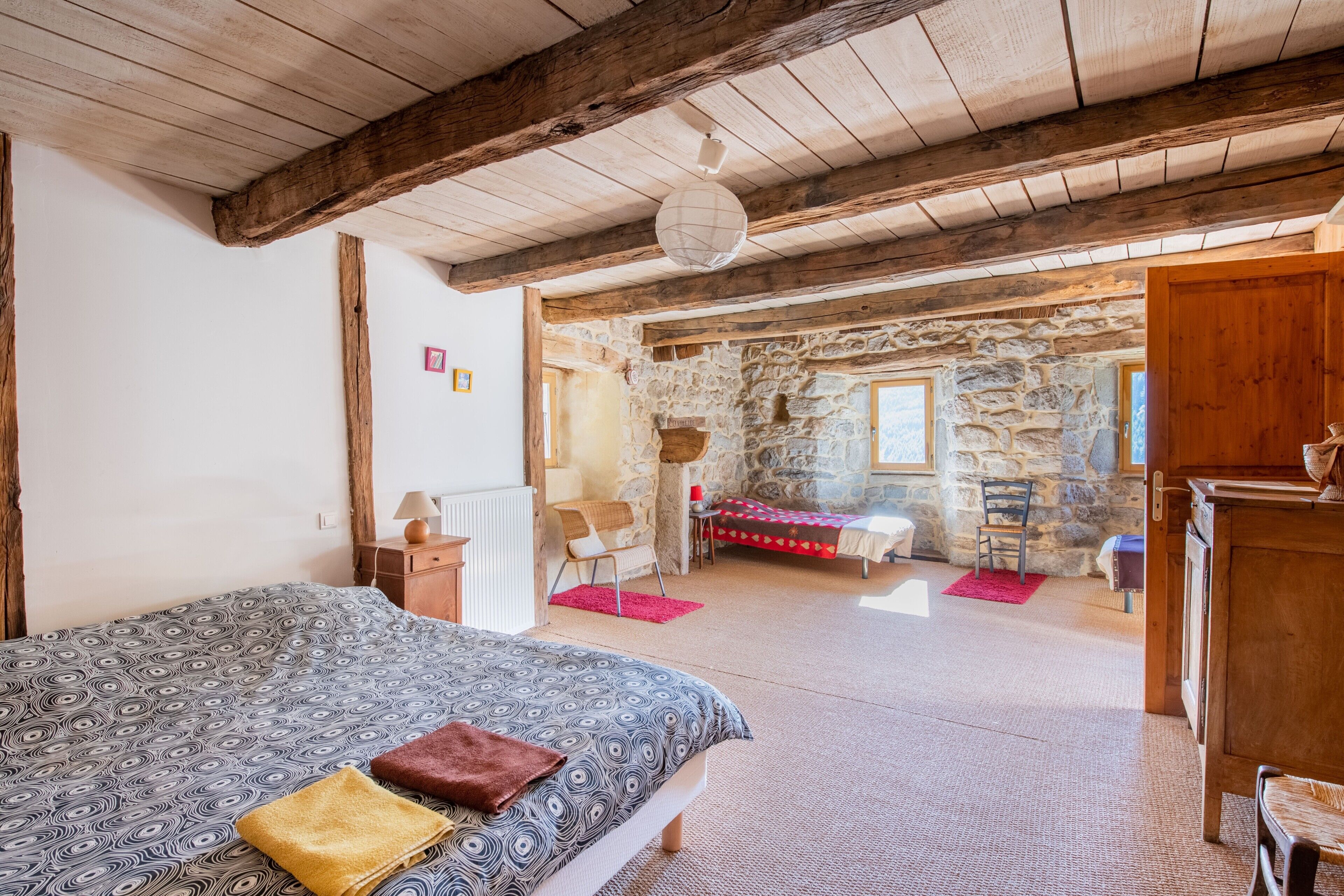 A bedroom with a bed, wooden beams, a stone wall, and a stone fireplace.