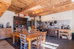 Una cocina rústica con vigas de madera, una mesa de comedor en el centro y diversos electrodomésticos.