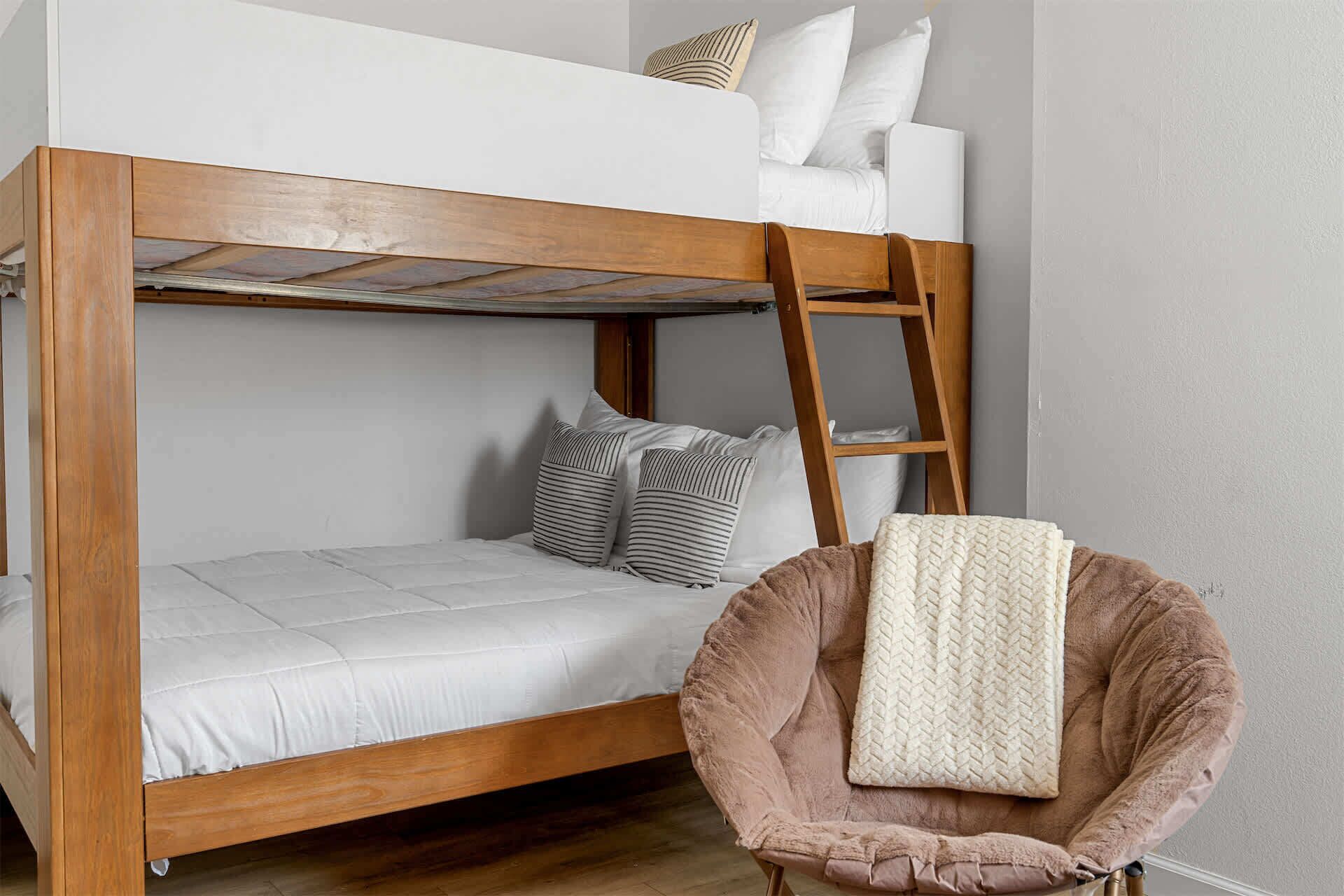 A bunk bed with a ladder, a chair with a blanket, and pillows.