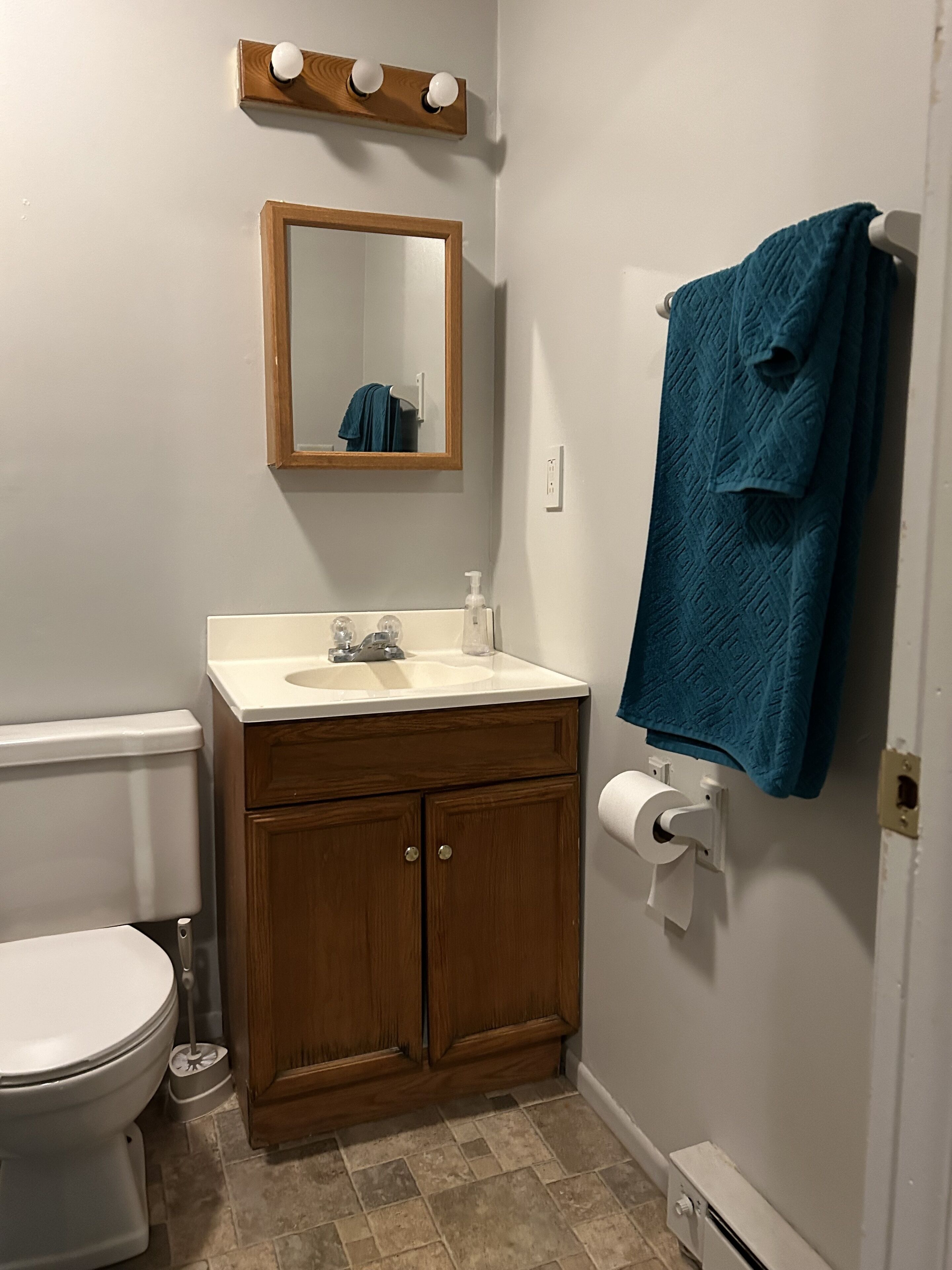 Ein Badezimmer mit Toilette, Waschbecken, Holzschrank, Spiegel, Handtuchhalter und Toilettenpapierhalter.