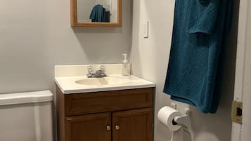 Une salle de bain comprenant des toilettes, un lavabo, un meuble en bois, un miroir, un porte-serviettes et un support à papier toilette.