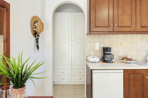 A kitchen with white cabinets, a coffee maker, a potted plant, and a door with a decorative hat.