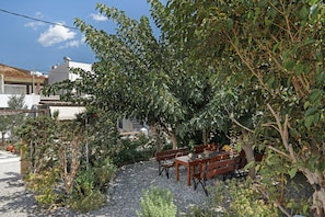 A patio with a table and benches, surrounded by trees and plants. - Apartment 'Studios Asterias  4' with Shared Terrace, Wi-Fi and Air Conditioning (Astipalea)