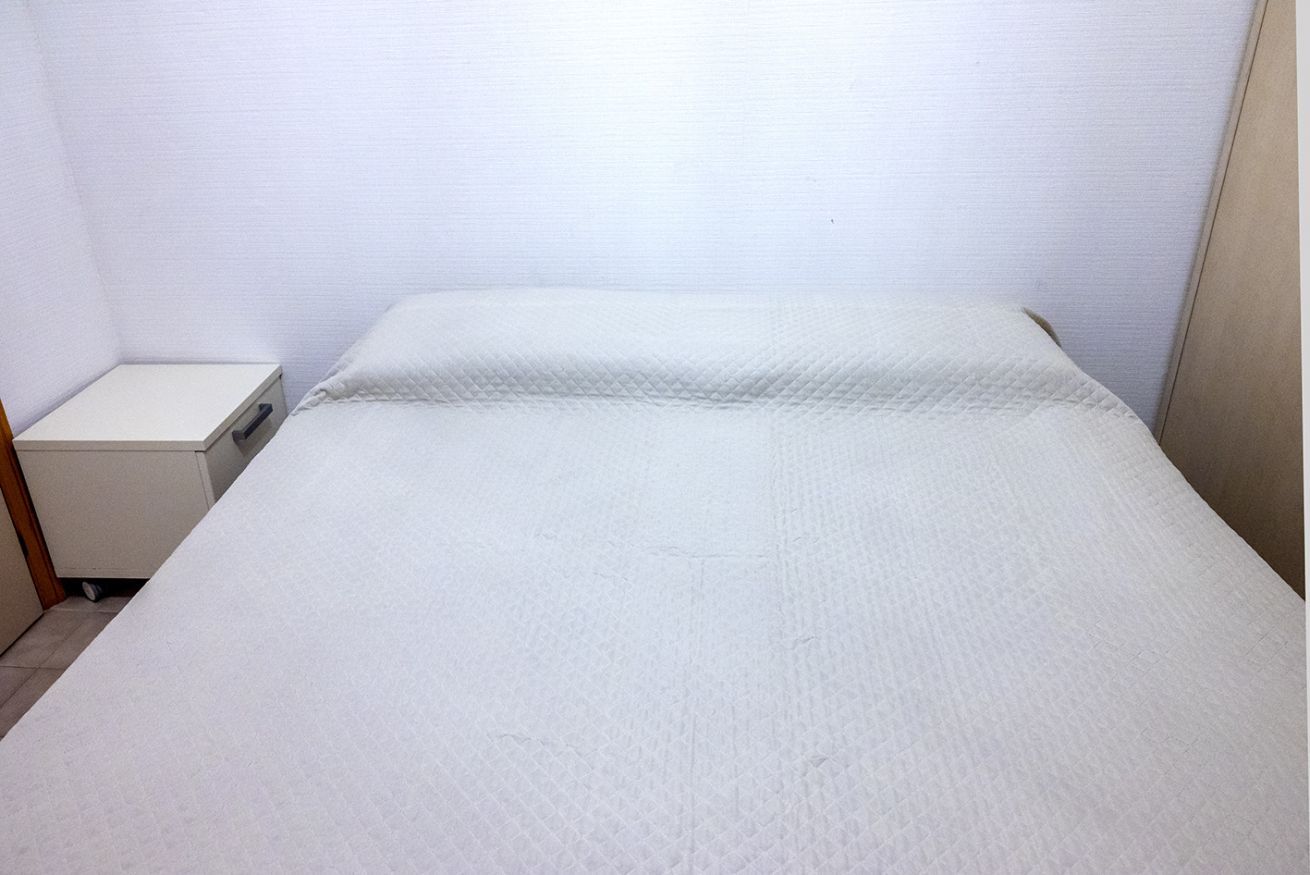 Une petite chambre avec un lit simple, un mur blanc uni et une table de chevet sobre.