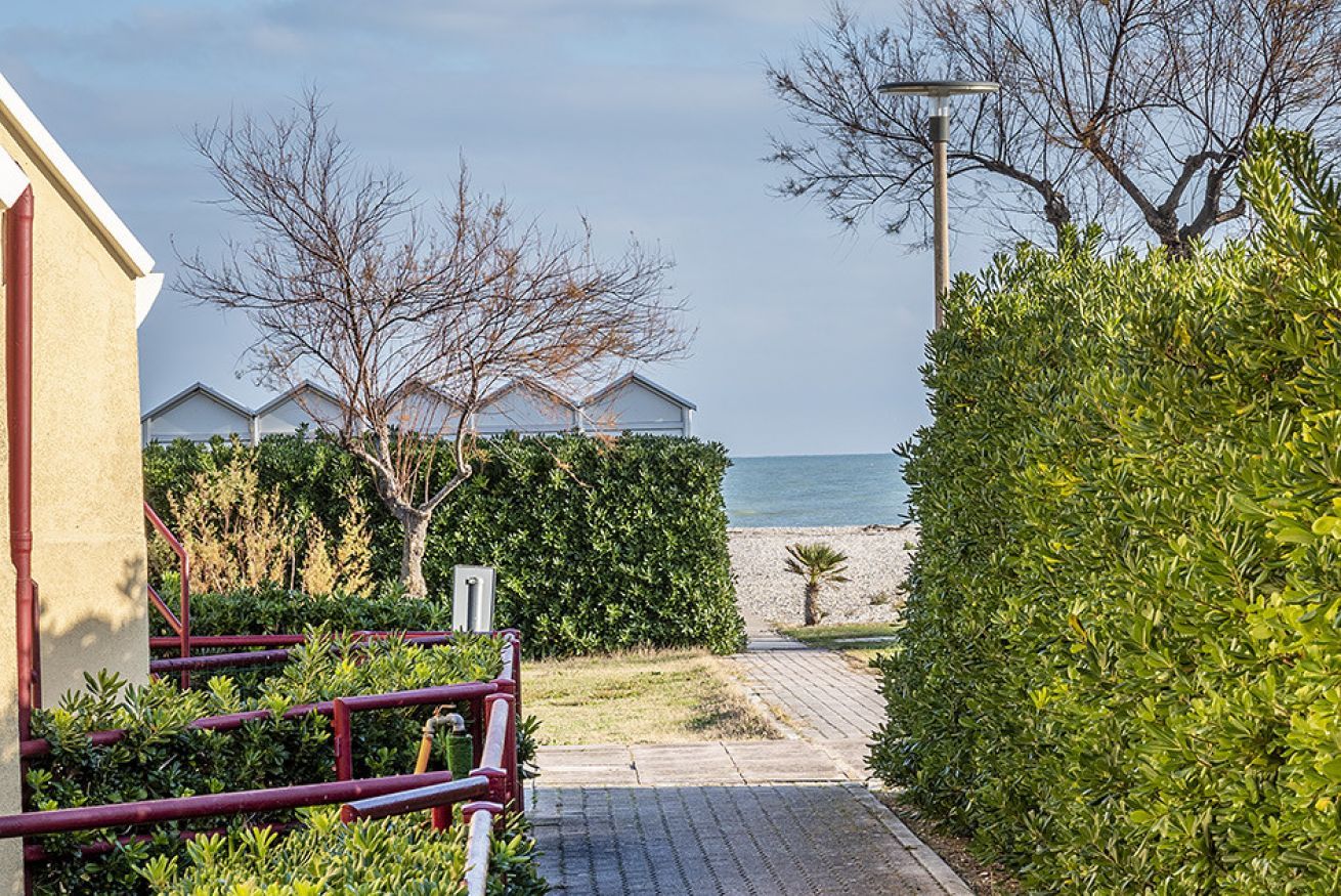 Un camino que lleva a una playa, con un edificio a la izquierda y un seto a la derecha.