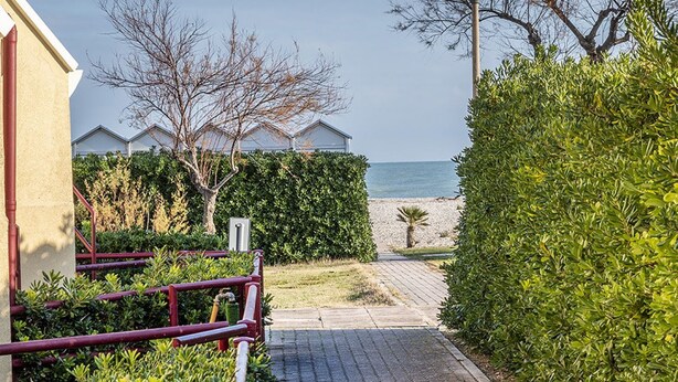 Un sentier qui mène à une plage, avec un bâtiment sur la gauche et une haie sur la droite.