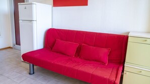 Un canapé rouge, un réfrigérateur blanc et un meuble jaune dans une pièce dont le sol est recouvert de carreaux.
