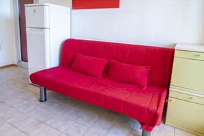Um sofá vermelho, um frigorífico branco e um armário amarelo numa divisão com soalho em mosaico.