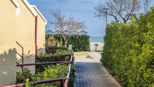 Un sendero que lleva a un edificio con vista al mar, rodeado de vegetación y un cielo despejado.