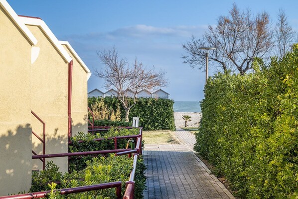 A pathway leading to a building with a view of the sea, surrounded by greenery and a clear sky.