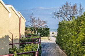 A pathway leading to a building with a view of the sea, surrounded by greenery and a clear sky.