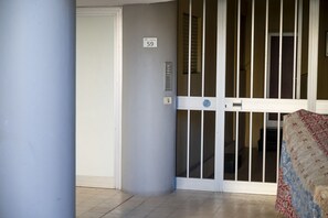 Entrada de hotel com porta numerada '59', teclado e porta de vidro deslizante.