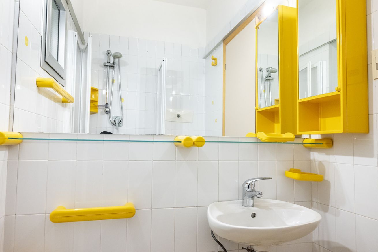 Une salle de bain avec une douche à parois de verre, un lavabo blanc et des étagères de rangement jaunes.