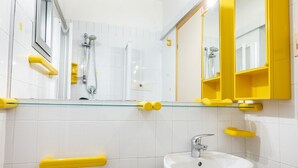 Une salle de bain avec une douche à parois de verre, un lavabo blanc et des étagères de rangement jaunes.