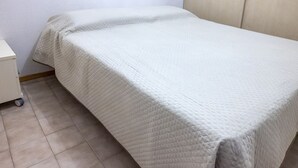 Una cama individual con cubrecolcha blanco acolchado, una mesita de noche pequeña y un mueble fijado a la pared.