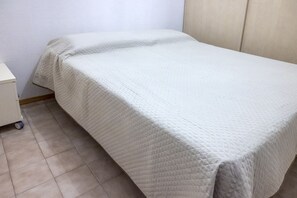 A single bed with a quilted white cover, a small bedside table, and a wall-mounted cabinet.