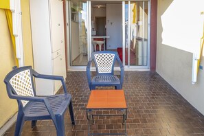 A patio with two chairs and a small table, a sliding glass door leading to an interior space, and a yellow wall on the left.