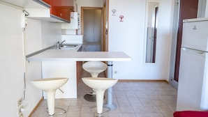 Una cocina compacta con encimera blanca, dos taburetes de bar, un lavabo y un refrigerador.