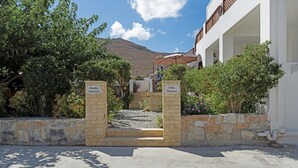 Ein Villa-Eingang mit einer Steinmauer, einer Treppe zu einem überdachten Bereich und einem Berg im Hintergrund.